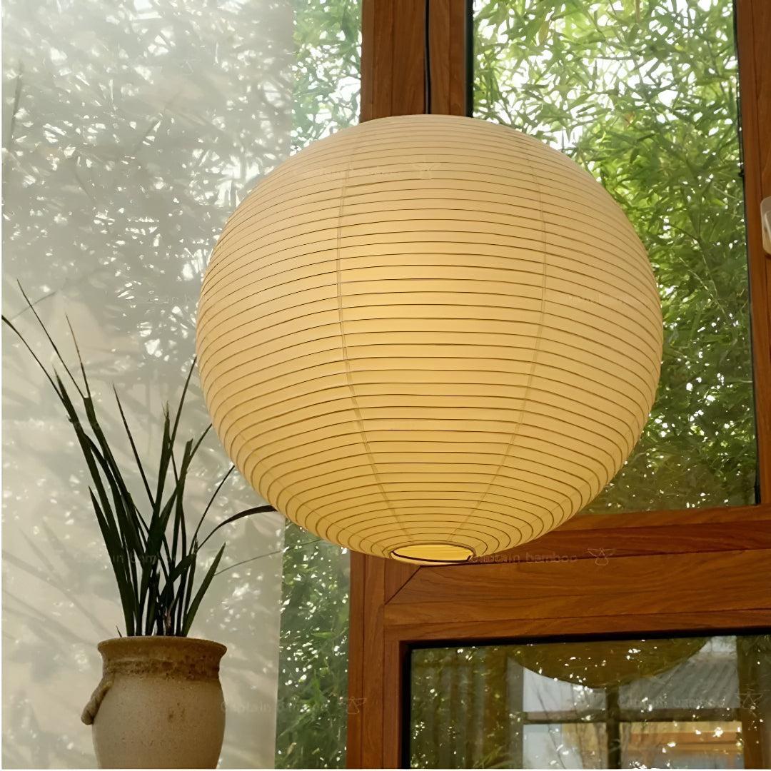Round rice paper lantern pendant casting warm Japandi glow near a window.